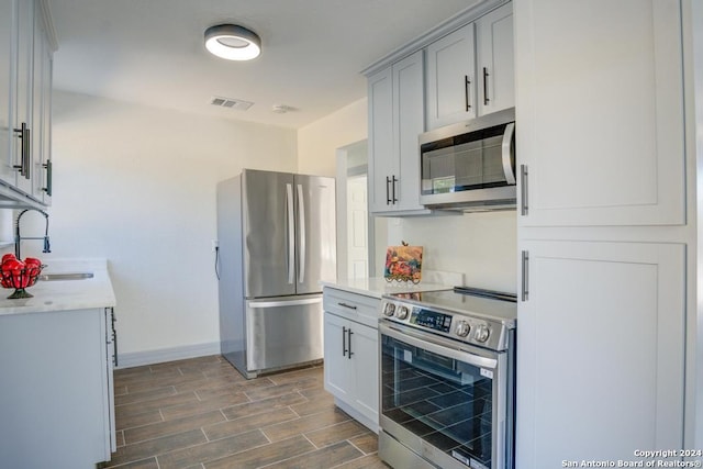 kitchen with light stone counters, dark hardwood / wood-style flooring, appliances with stainless steel finishes, gray cabinetry, and sink