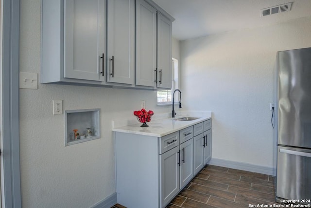 kitchen with gray cabinetry, sink, dark wood-type flooring, and stainless steel refrigerator