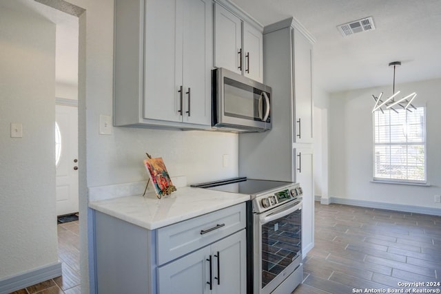 kitchen featuring light stone countertops, hardwood / wood-style floors, appliances with stainless steel finishes, and a notable chandelier