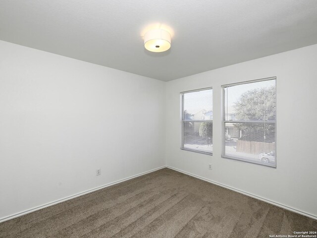 unfurnished room with dark carpet and baseboards