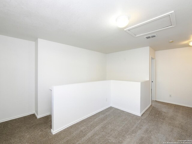 unfurnished room with attic access, carpet floors, and baseboards