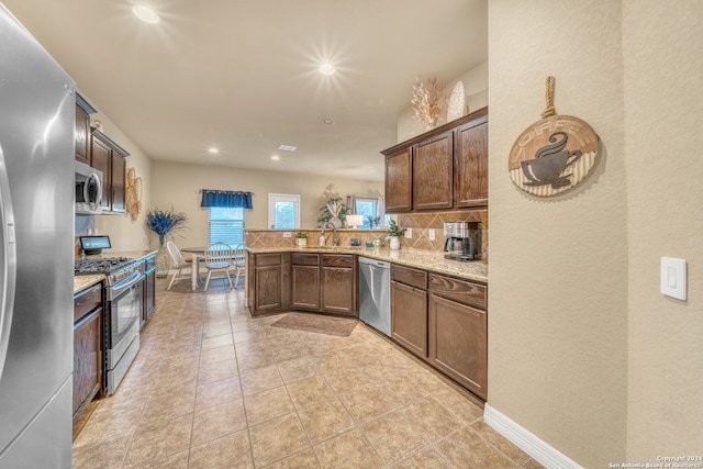 kitchen with decorative backsplash, kitchen peninsula, stainless steel appliances, sink, and light stone countertops