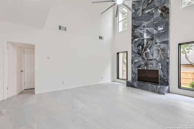 unfurnished living room with a tiled fireplace, a high ceiling, and ceiling fan