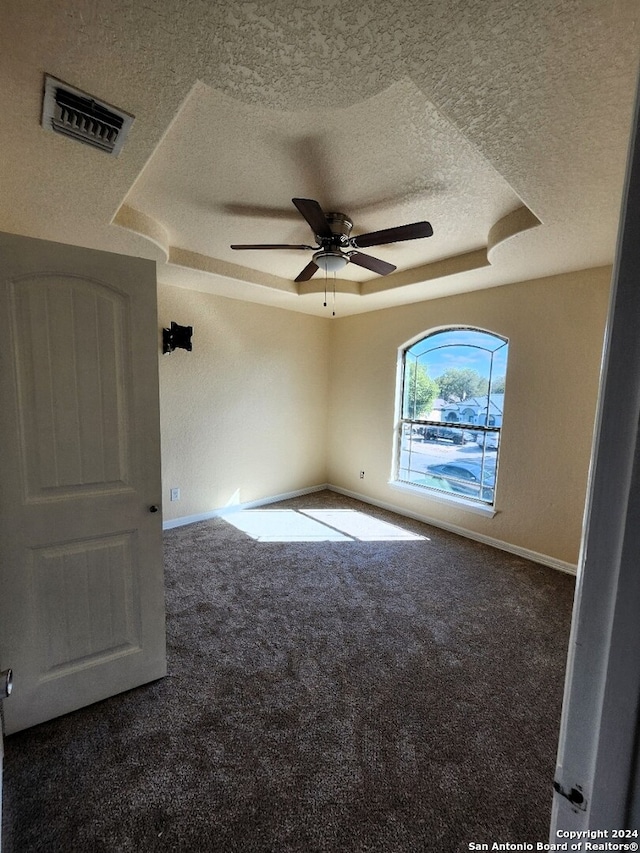 carpeted spare room featuring a textured ceiling, ceiling fan, and a raised ceiling