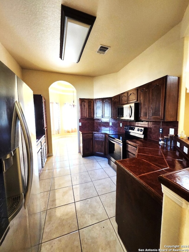 kitchen with a textured ceiling, appliances with stainless steel finishes, dark brown cabinets, and light tile patterned flooring