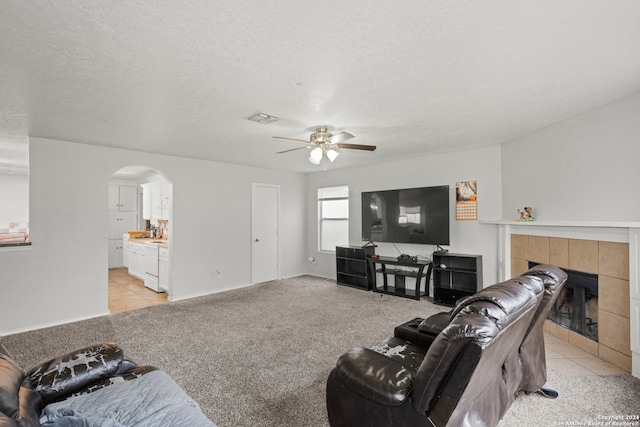 carpeted living room featuring a textured ceiling, a tile fireplace, and ceiling fan