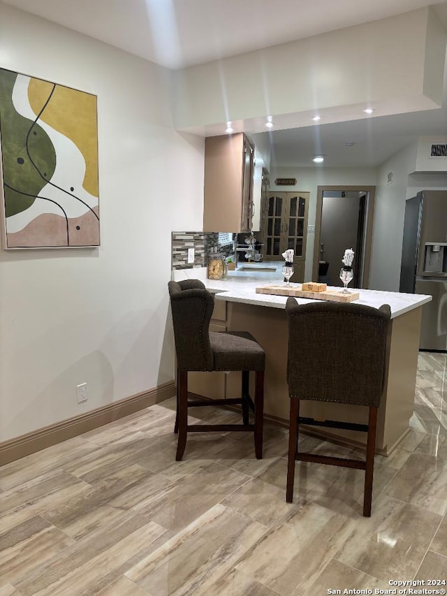 interior space with light wood-type flooring, a breakfast bar, kitchen peninsula, and stainless steel refrigerator with ice dispenser