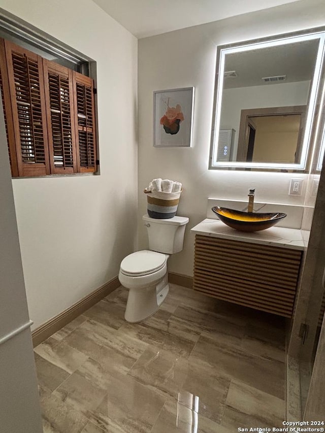 half bath featuring toilet, visible vents, vanity, and baseboards