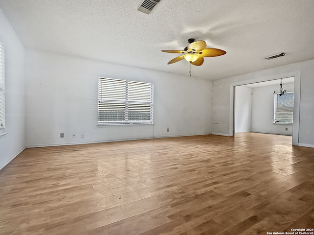 spare room featuring ceiling fan with notable chandelier, a textured ceiling, and light hardwood / wood-style floors