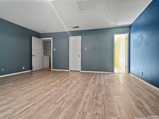 unfurnished bedroom featuring a textured ceiling, ensuite bathroom, and light wood-type flooring