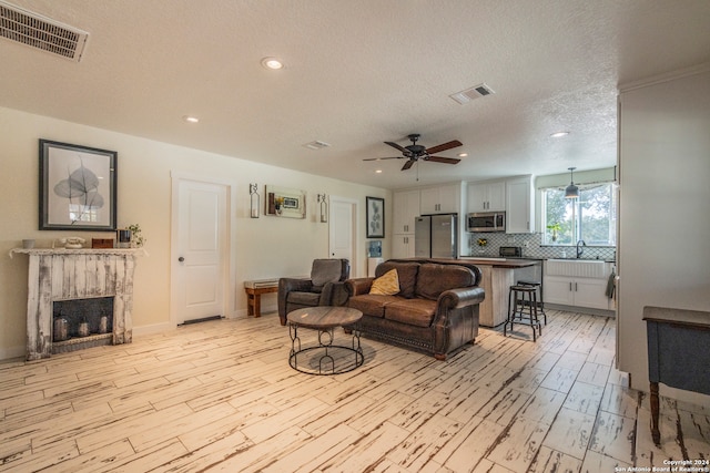 living room featuring ceiling fan, a textured ceiling, and light hardwood / wood-style floors