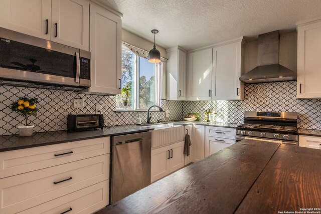 kitchen featuring white cabinetry, stainless steel appliances, wall chimney exhaust hood, decorative light fixtures, and decorative backsplash