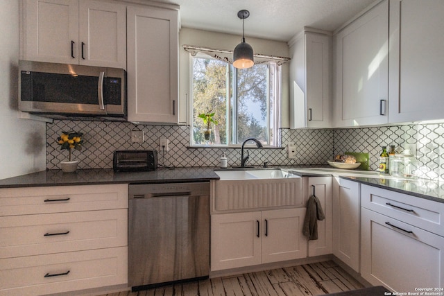 kitchen featuring stainless steel appliances, sink, pendant lighting, white cabinets, and tasteful backsplash