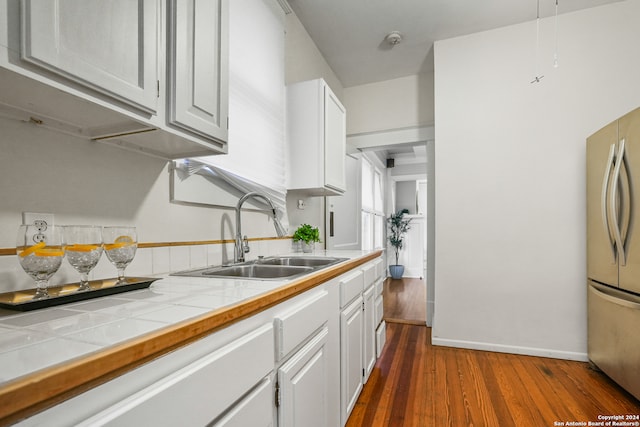 kitchen with sink, white cabinetry, tile counters, stainless steel refrigerator, and dark hardwood / wood-style floors