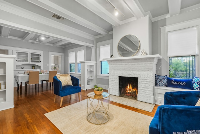 living room with hardwood / wood-style floors, beamed ceiling, track lighting, and a fireplace