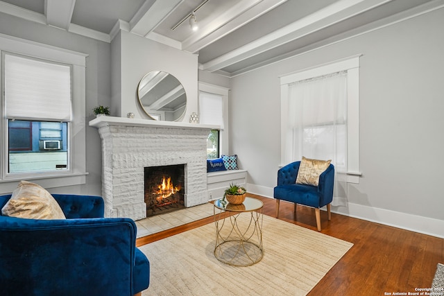 sitting room with beam ceiling, wood-type flooring, track lighting, and a brick fireplace