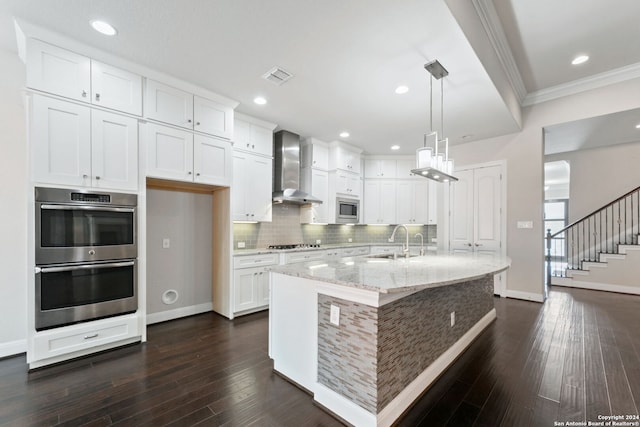 kitchen with white cabinetry, wall chimney exhaust hood, appliances with stainless steel finishes, and a center island with sink