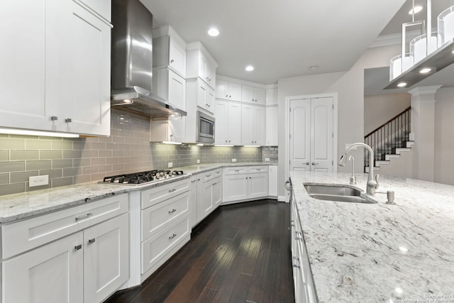 kitchen featuring wall chimney range hood, sink, white cabinets, light stone counters, and dark hardwood / wood-style floors