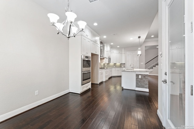 kitchen featuring dark wood-type flooring, white cabinetry, a center island with sink, and pendant lighting