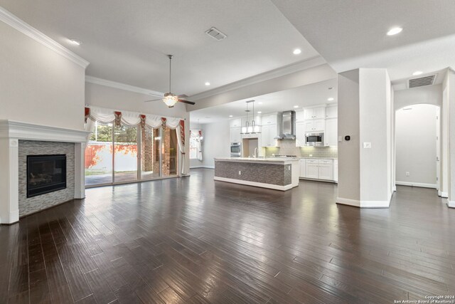 unfurnished living room with crown molding, a fireplace, dark hardwood / wood-style floors, and ceiling fan