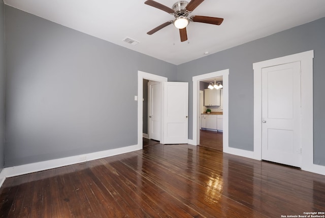 unfurnished bedroom featuring dark wood-type flooring, ensuite bathroom, and ceiling fan with notable chandelier