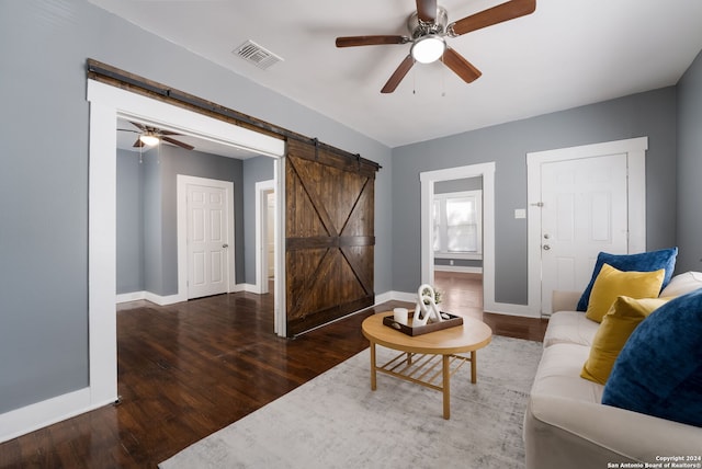 living room with dark wood-type flooring, ceiling fan, and a barn door