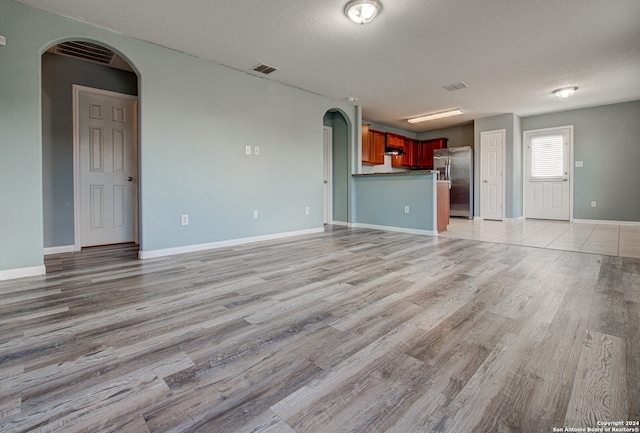 unfurnished living room with light hardwood / wood-style flooring and a textured ceiling