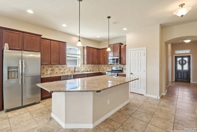 kitchen featuring appliances with stainless steel finishes, light stone counters, a kitchen island, and backsplash