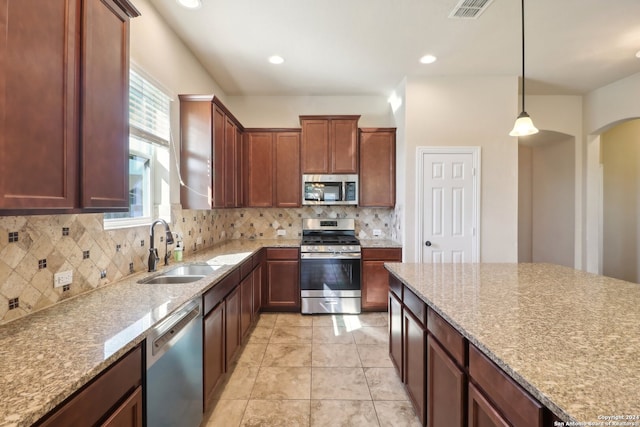 kitchen with light stone counters, stainless steel appliances, sink, and hanging light fixtures