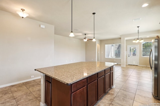 kitchen with stainless steel fridge, a kitchen island, ceiling fan with notable chandelier, decorative light fixtures, and light stone counters