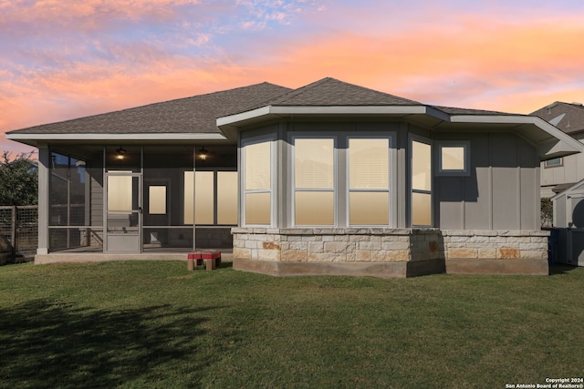 back house at dusk with a yard and a sunroom