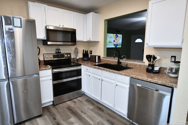 kitchen featuring white cabinets, hardwood / wood-style floors, appliances with stainless steel finishes, dark stone counters, and sink