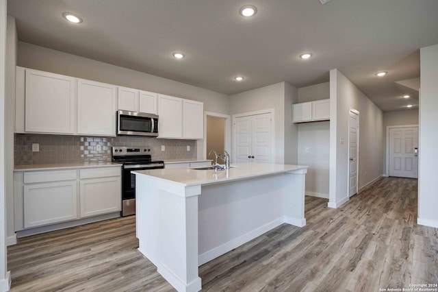 kitchen with white cabinetry, a kitchen island with sink, light wood-type flooring, and appliances with stainless steel finishes