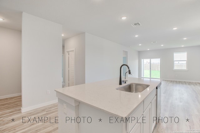 kitchen with light hardwood / wood-style flooring, a kitchen island with sink, sink, and light stone counters