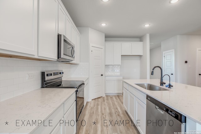 kitchen with sink, light wood-type flooring, white cabinetry, stainless steel appliances, and light stone counters