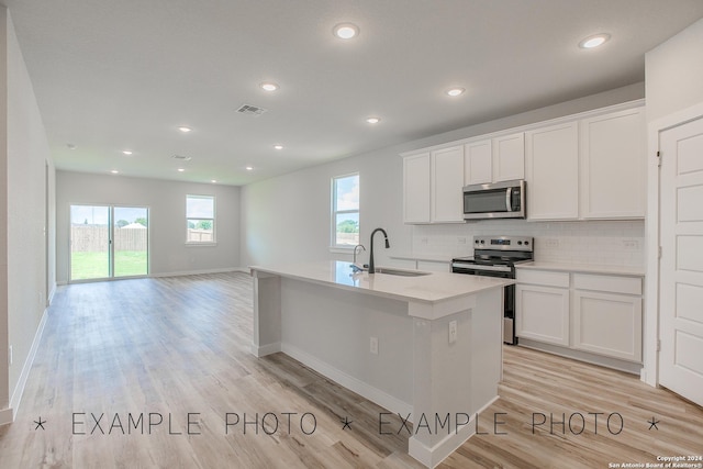 kitchen with white cabinets, a center island with sink, sink, light hardwood / wood-style floors, and stainless steel appliances