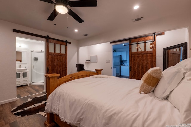 bedroom featuring ensuite bathroom, a barn door, stainless steel fridge, ceiling fan, and dark hardwood / wood-style floors