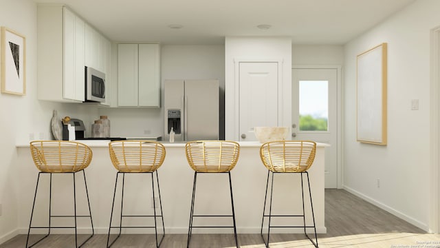 kitchen with a breakfast bar area, light wood-type flooring, refrigerator with ice dispenser, and white cabinets