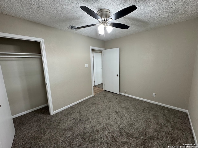 unfurnished bedroom featuring dark colored carpet, a textured ceiling, and ceiling fan