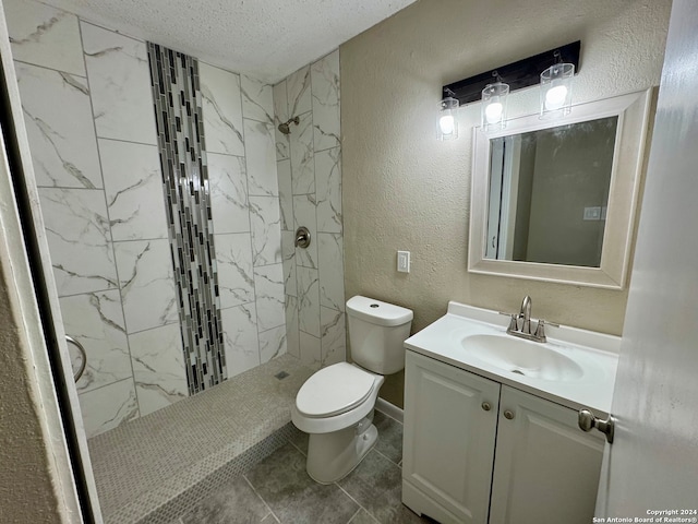 bathroom featuring a textured ceiling, toilet, tile patterned floors, tiled shower, and vanity