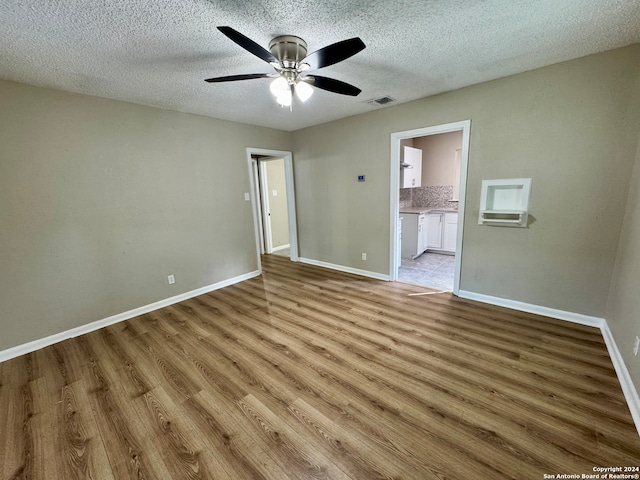 unfurnished bedroom featuring connected bathroom, ceiling fan, a textured ceiling, and light hardwood / wood-style flooring