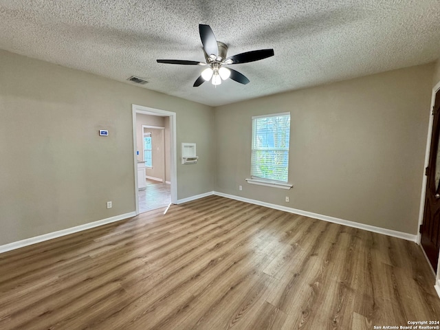 spare room with ceiling fan, an AC wall unit, a textured ceiling, and light wood-type flooring