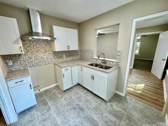 kitchen with sink, ceiling fan, light hardwood / wood-style floors, wall chimney exhaust hood, and white cabinets