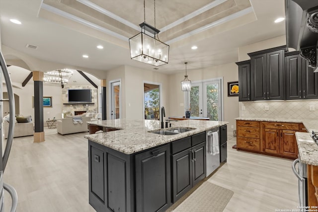 kitchen featuring decorative backsplash, sink, a center island with sink, and a raised ceiling