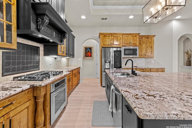 kitchen featuring light stone countertops, sink, stainless steel appliances, range hood, and decorative backsplash