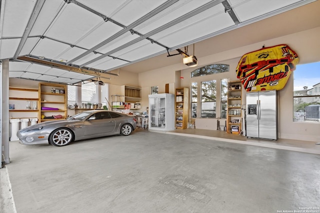 garage with a garage door opener and stainless steel refrigerator with ice dispenser