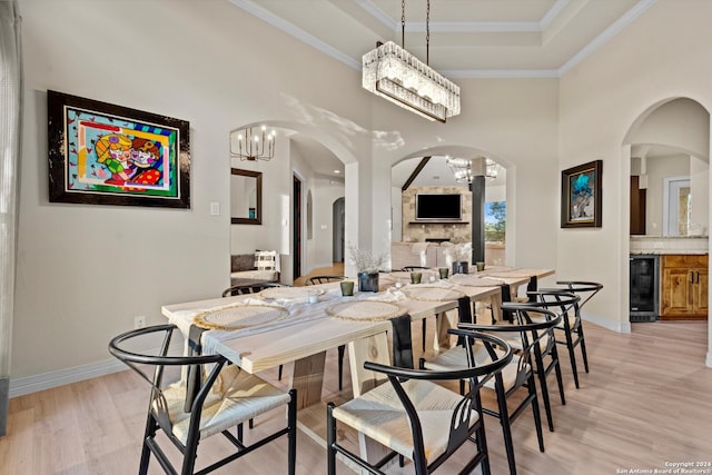 dining room featuring light hardwood / wood-style floors, wine cooler, ornamental molding, a fireplace, and a towering ceiling