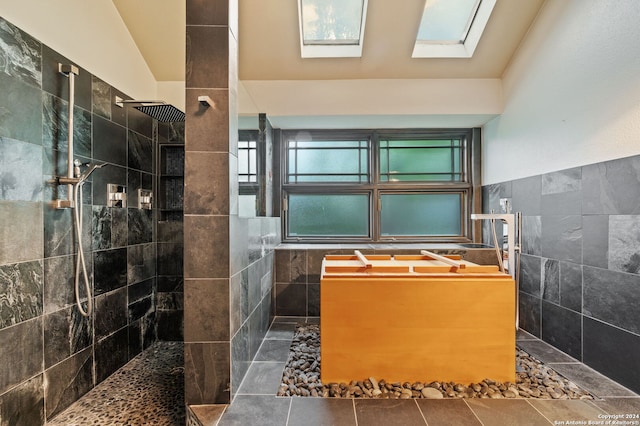 bathroom with tile walls, lofted ceiling with skylight, a tile shower, and tile patterned floors