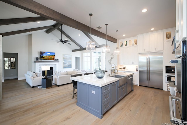 kitchen with pendant lighting, sink, appliances with stainless steel finishes, a kitchen island with sink, and white cabinets