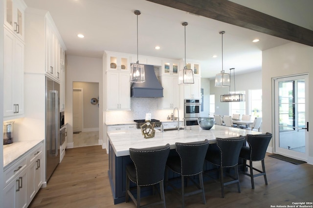 kitchen with dark wood-type flooring, beam ceiling, custom exhaust hood, white cabinetry, and a large island